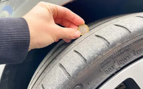 Una mano tiene una moneta da 1 euro per mostrare quanti mm di battistrada ha un pneumatico nuovo. Il battistrada è usurato.