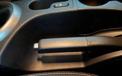 Maniglia del freno di servizio in un'auto, con portabicchieri e pulsante di blocco nelle vicinanze.