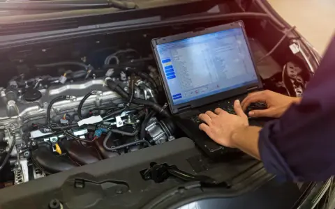Meccanico controlla il motore di un'auto con un laptop, analizzando dati per ottimizzare l'anticipo automatico motori diesel.