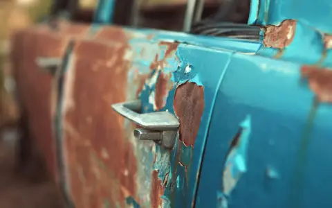 Portiera di un'auto blu con vernice scrostata e ruggine evidente. Un lavoro di restauro per togliere la ruggine sarebbe necessario per riportarla al suo antico splendore.