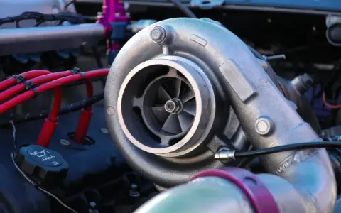 Dettaglio di un motore con un turbo benzina cromato, cavi rossi e un tappo dell'olio.