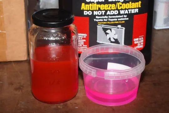 Barattolo con liquido radiatore rosso e contenitore con liquido rosa. La differenza liquido radiatore rosso e blu è visibile, uno è rosso vivo, l'altro rosa.