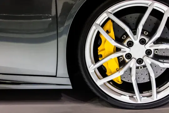 Dettaglio di un'auto sportiva con cerchi in lega argentati e pinze freni gialle appena verniciate.
