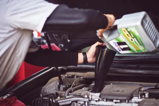 Persona effettua il rabbocco olio motore versando olio da una tanica Mobil in un imbuto.