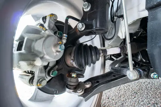 Dettaglio del sistema frenante e della sospensione di un'auto, con particolare attenzione all'asse della macchina, al giunto omocinetico e al braccio oscillante.