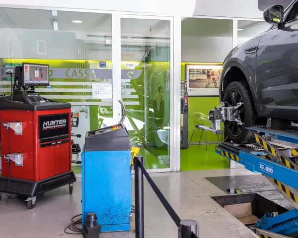 Attrezzatura per la convergenza gomme in officina. Un'auto è sollevata su un ponte, con sensori applicati alla ruota.