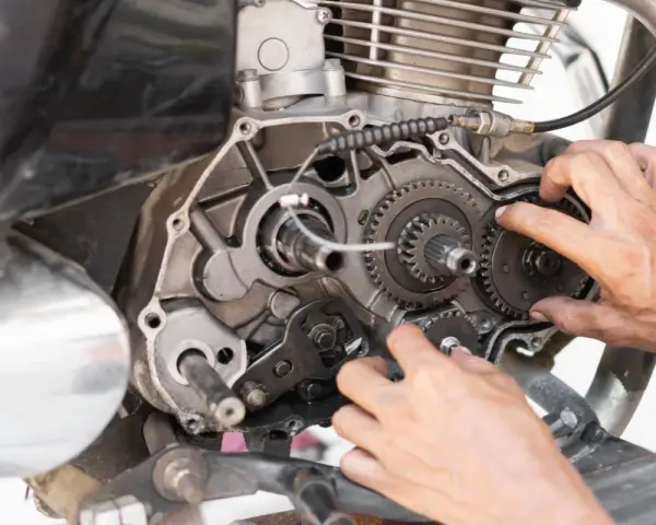 Mani che lavorano sul cambio di una moto, forse per risolvere una perdita di potenza auto benzina. Ingranaggi e meccanismi a vista.