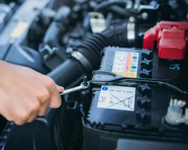 Mano con chiave inglese che lavora sulla batteria dell'auto. La batteria si scarica a vettura ferma, un problema comune per le auto con sistema Start & Stop.