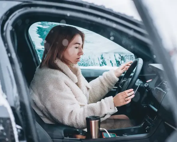 Donna al volante in un'auto coperta di neve, con le mani sul volante. Impara come guidare sulla neve in sicurezza.