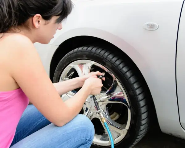 Donna controlla la pressione pneumatici auto, gonfiando la ruota con un compressore.