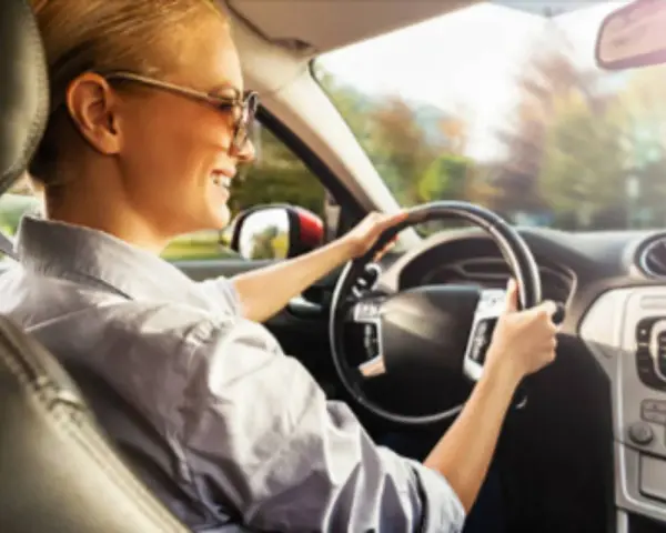 Donna sorridente guida con il volante che vibra a bassa velocità, godendosi il sole del mattino.