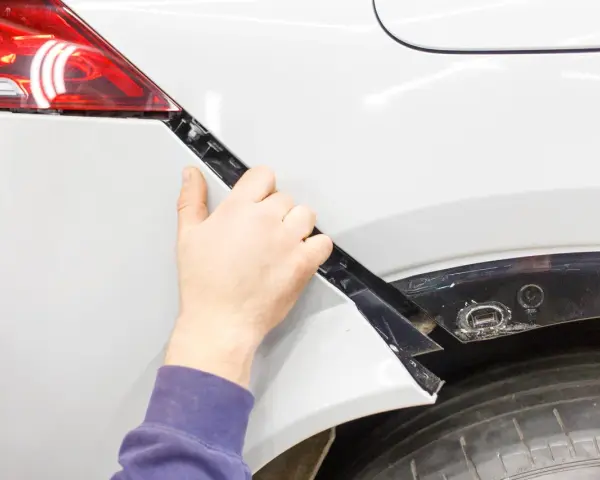 Mano che lavora alla riparazione paraurti in plastica di un'auto bianca.