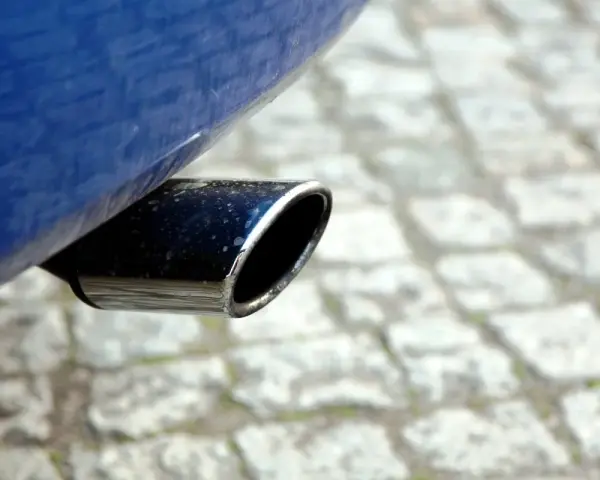 Il tubo di scarico cromato di un'auto blu, parte del silenziatore che attutisce il rumore del motore, su un selciato.