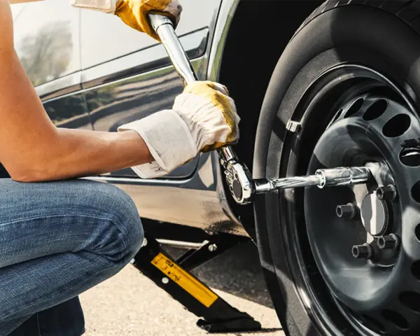 Persona con guanti gialli usa una chiave per serrare i bulloni della ruota di un'auto sollevata da un cric. Il significato di "nm" è la coppia di serraggio.