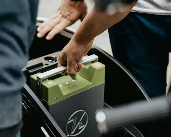 Mani che inseriscono una batteria verde in un vano. La durata della batteria della macchina è fondamentale per l'autonomia.