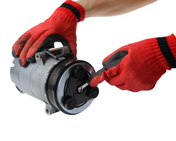 Mani guantate rosse lavorano su un compressore per la sostituzione del compressore aria condizionata auto.