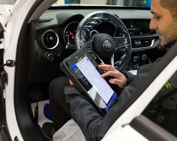 Meccanico usa tablet per diagnosticare la centralina auto. Il dispositivo mostra le opzioni di controllo e i dati del veicolo.