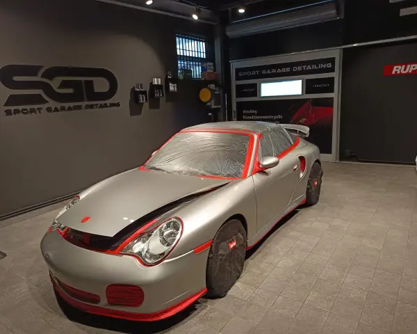 Auto sportiva pronta per la verniciatura, con protezioni rosse e cellophane. Il logo "SGD Sport Garage Detailing" è visibile.
