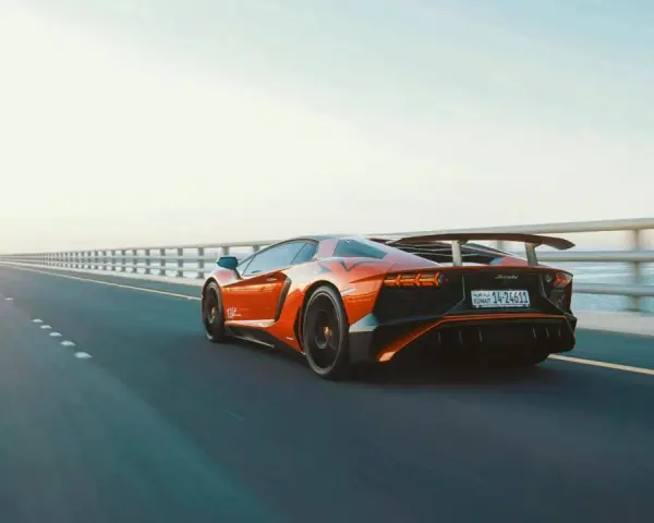 Arancia Lamborghini sfreccia su un ponte, i suoi cavalli scatenati sull'asfalto. L'auto sportiva domina la scena, un'icona di velocità.