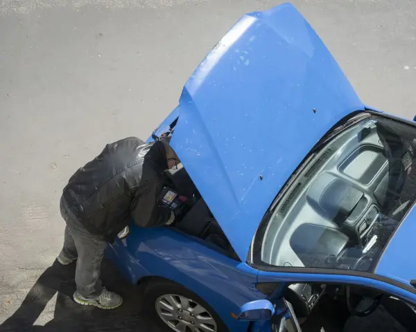 Uomo con giacca in pelle controlla la **macchina ferma** con il cofano aperto, forse un problema alla **batteria**.
