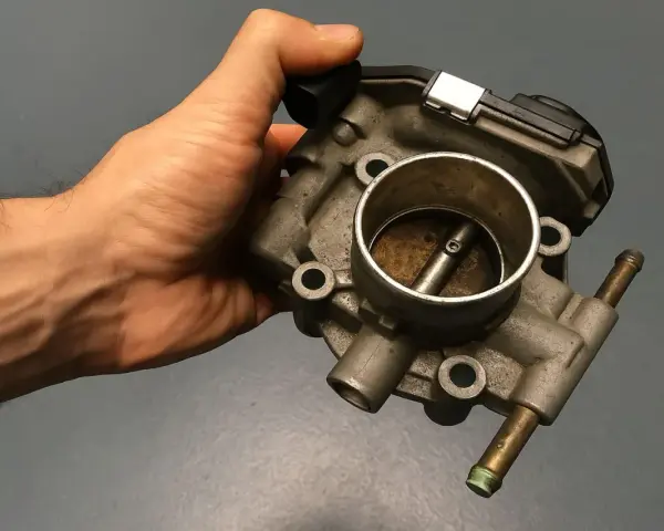 Mano che tiene una valvola a farfalla motore benzina, componente essenziale per il controllo del flusso d'aria.