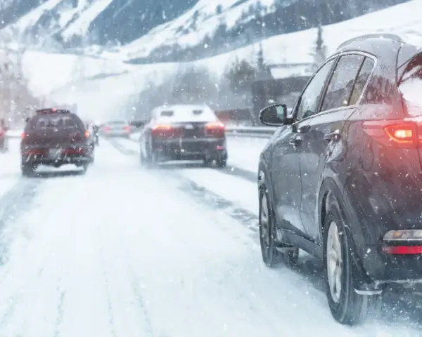 Auto con trazione posteriore sulla neve, luci accese, in un paesaggio montano innevato.