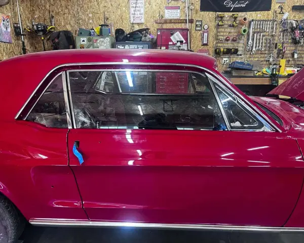 Auto d'epoca con vernice rosso candy apple lucida, in un garage con attrezzi appesi.