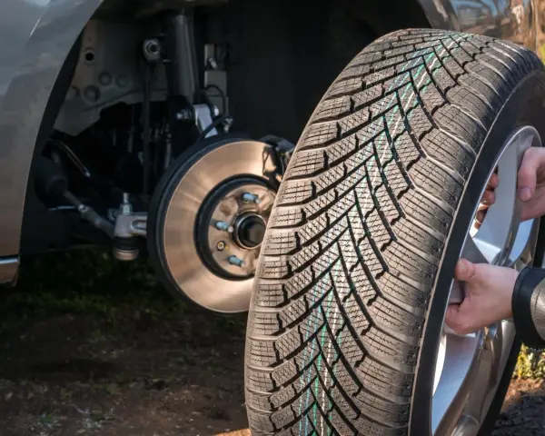 Mani che montano una gomma nuova su un cerchio, con il mozzo dell'auto visibile. La rotazione gomme auto è fondamentale per l'usura uniforme.