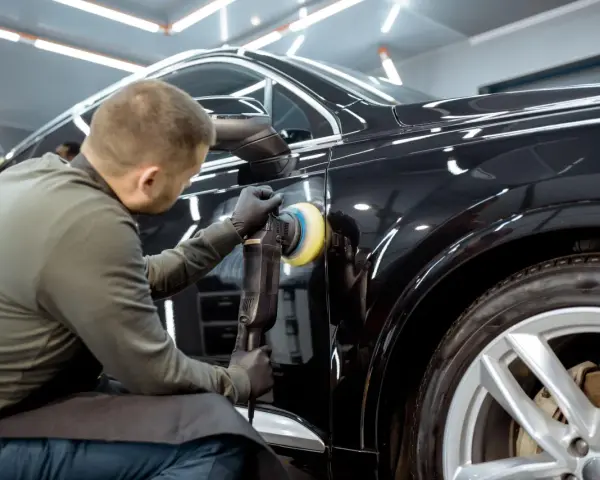 Dettaglio di un professionista che lucida una carrozzeria metallizzata nera per eliminare graffi, con lucidatrice rotativa.