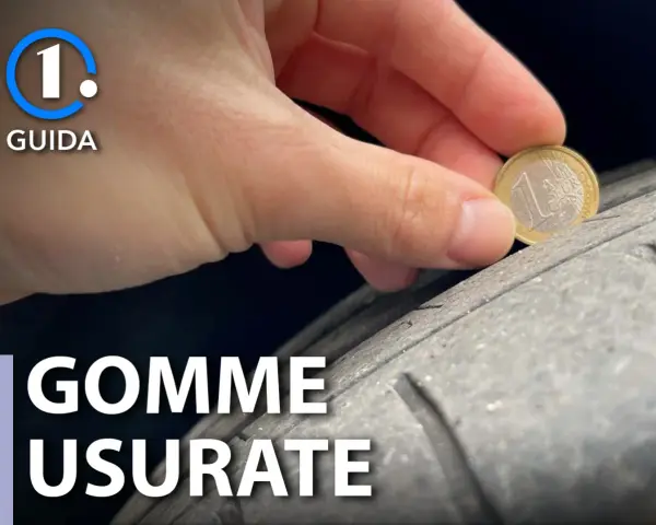 Una mano tiene una moneta da 1 euro per controllare l'usura di una gomma. Gomme lisce come capire quando cambiarle.