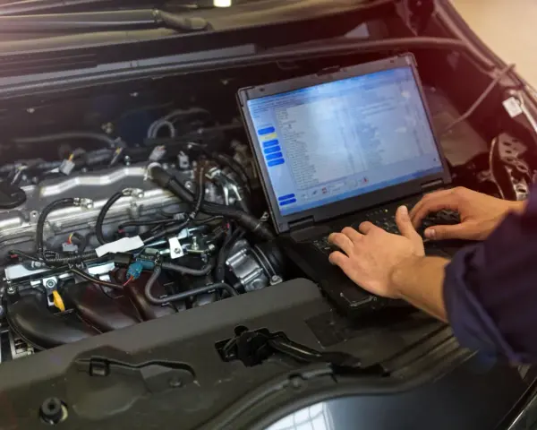 Meccanico controlla il motore di un'auto con un laptop, analizzando dati per ottimizzare l'anticipo automatico motori diesel.