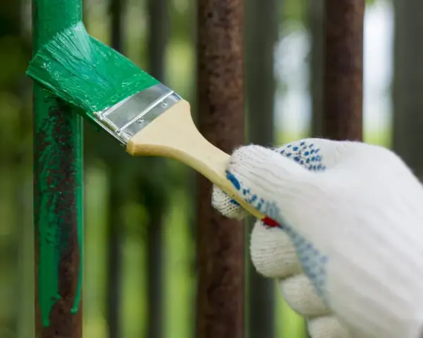 Mano guantata che inizia a verniciare ferro arrugginito con vernice verde brillante, dando nuova vita a una vecchia ringhiera.