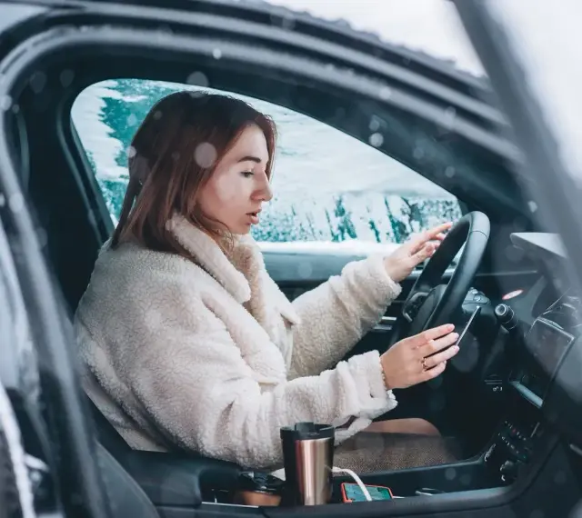 Donna al volante in un'auto coperta di neve, con le mani sul volante. Impara come guidare sulla neve in sicurezza.