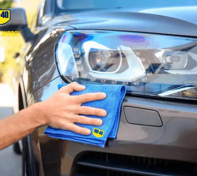 Mano che lucida fari auto con WD-40 e panno blu. Ottimo lavoro!