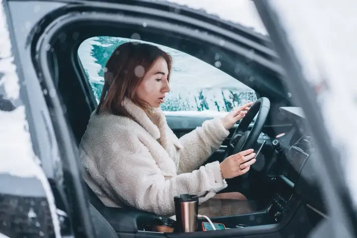 Donna al volante in un'auto coperta di neve, con le mani sul volante. Impara come guidare sulla neve in sicurezza.