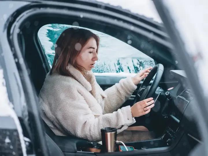 Donna al volante in un'auto coperta di neve, con le mani sul volante. Impara come guidare sulla neve in sicurezza.