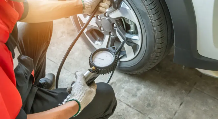 Controllo pressione gomme: il manometro indica pressione gomme troppo alta. Un meccanico con guanti sta verificando la pressione di un pneumatico.