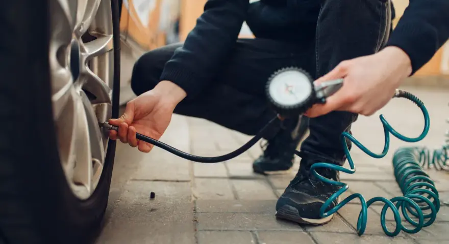 Persona controlla la pressione degli pneumatici dell'auto con un manometro, seguendo la tabella pressione pneumatici auto per la sicurezza.