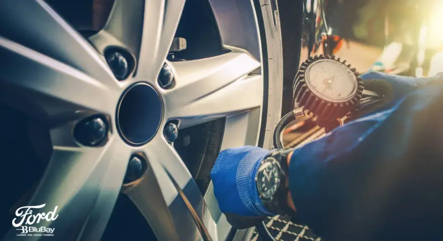 Controllo pneumatici con manometro su cerchio Ford. Guanto blu e orologio da polso.