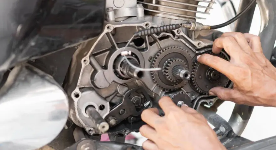 Mani che lavorano sul cambio di una moto, forse per risolvere una perdita di potenza auto benzina. Ingranaggi e meccanismi a vista.