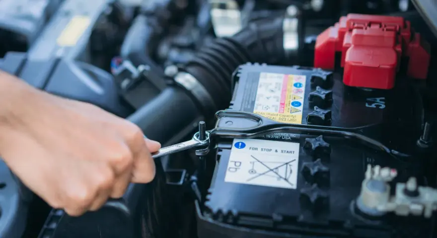 Mano con chiave inglese che lavora sulla batteria dell'auto. La batteria si scarica a vettura ferma, un problema comune per le auto con sistema Start & Stop.