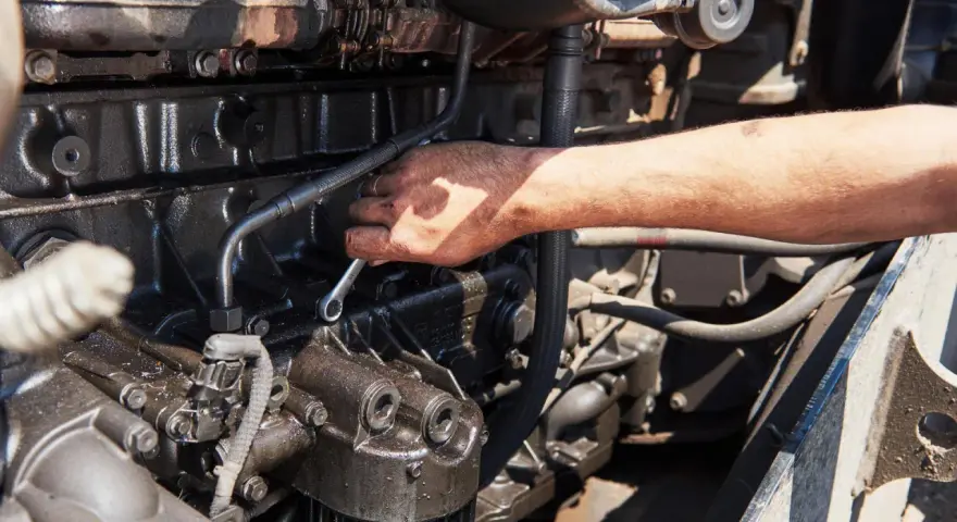 Mano con chiave inglese lavora su un motore sporco d'olio, forse per riparare cos'è l'alternatore.