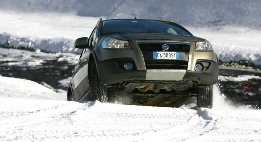 Un'auto con gomme invernali neve affronta un pendio innevato, sollevando spruzzi di bianco.