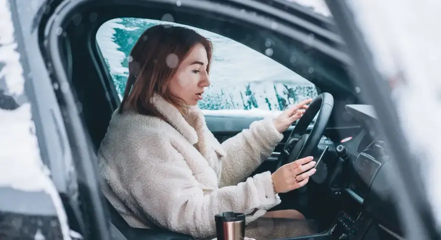 Donna al volante in un'auto coperta di neve, con le mani sul volante. Impara come guidare sulla neve in sicurezza.