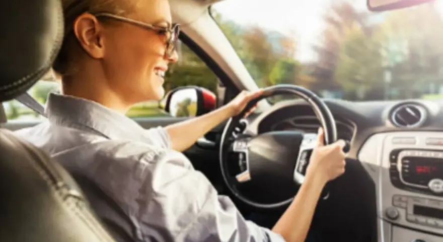 Donna sorridente guida con il volante che vibra a bassa velocità, godendosi il sole del mattino.