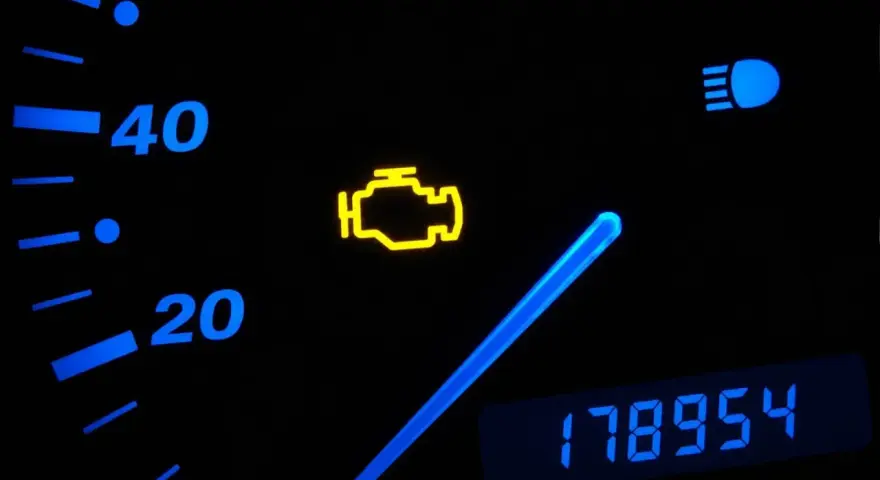 Cruscotto auto con spia motore accesa, indicatore di velocità e chilometraggio.