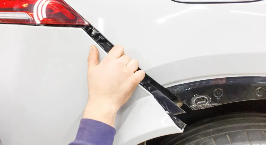 Mano che lavora alla riparazione paraurti in plastica di un'auto bianca.