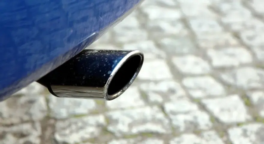 Il tubo di scarico cromato di un'auto blu, parte del silenziatore che attutisce il rumore del motore, su un selciato.