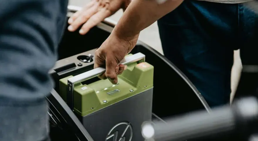 Mani che inseriscono una batteria verde in un vano. La durata della batteria della macchina è fondamentale per l'autonomia.