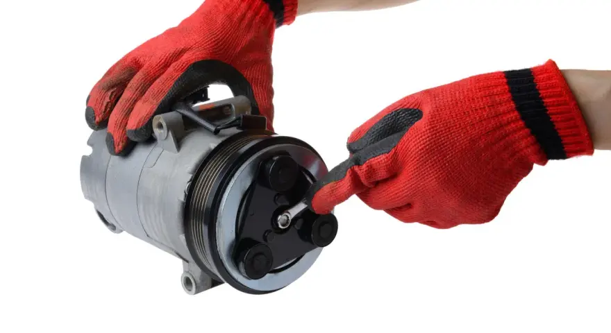 Mani guantate rosse lavorano su un compressore per la sostituzione del compressore aria condizionata auto.